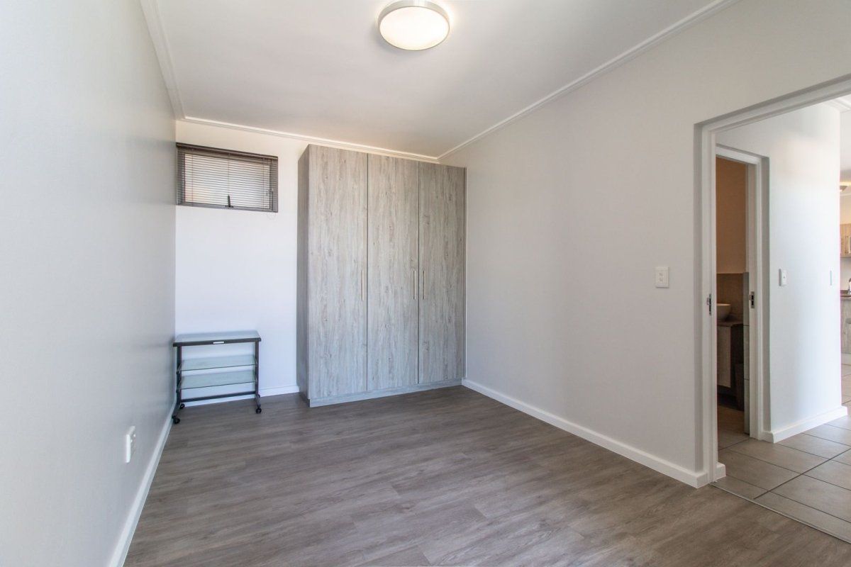 A clean, empty bedroom featuring modern laminate flooring, a built-in wardrobe, and a small high-level window, offering a neutral space ready for personalization.