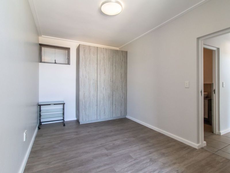 A clean, empty bedroom featuring modern laminate flooring, a built-in wardrobe, and a small high-level window, offering a neutral space ready for personalization.