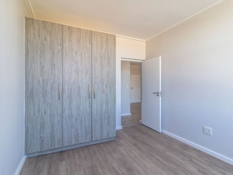 A bright, empty bedroom featuring modern wood-look laminate flooring and built-in cupboards, offering a clean and neutral space ready for personalization.