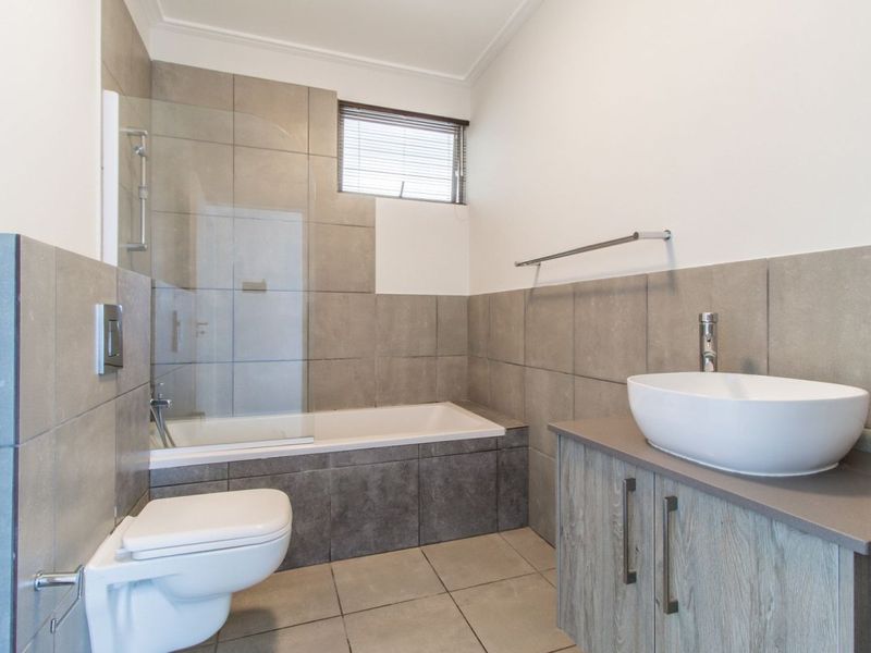 Modern bathroom featuring a wall-mounted toilet, built-in bathtub with glass screen, and a vanity cabinet with a vessel sink.