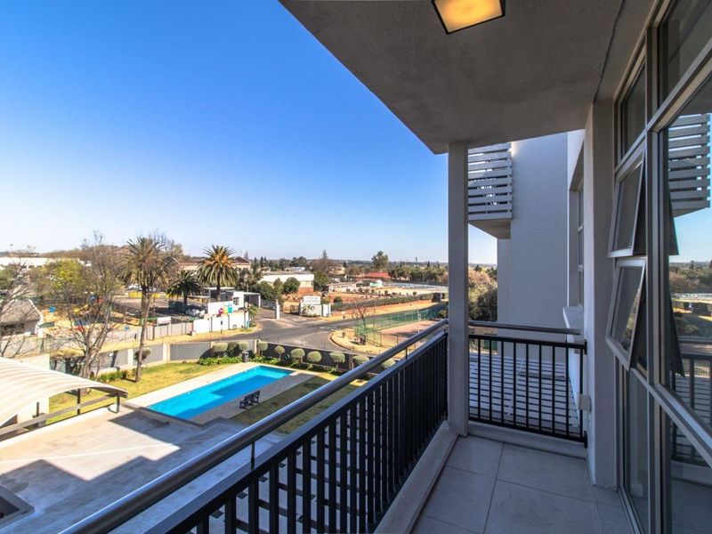 A spacious covered balcony featuring tiled flooring and a metal balustrade, offering elevated views over the complex pool and surrounding neighborhood.