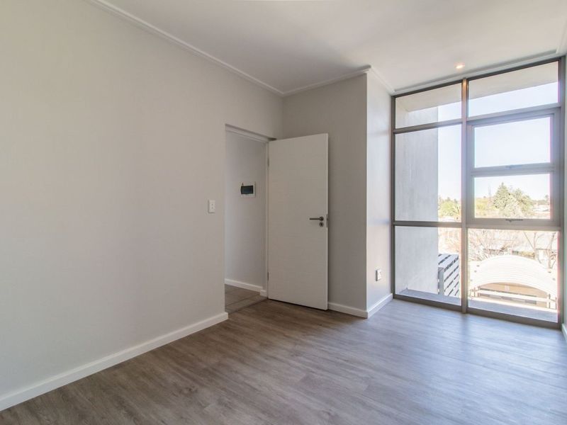 A bright and spacious bedroom featuring modern laminate flooring and large floor-to-ceiling windows that provide ample natural light.