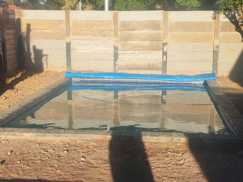 Outdoor swimming pool area featuring a tiled coping and a precast concrete boundary wall, currently requiring landscaping completion around the pool perimeter.