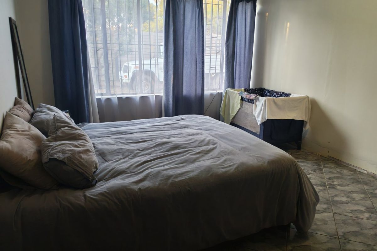 A bedroom featuring tiled flooring and large windows with security bars, providing natural light.