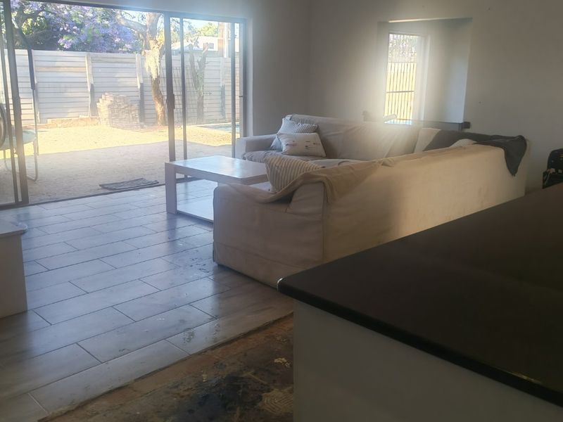 Open plan living area featuring large sliding doors to the garden and a kitchen island, currently requiring flooring repairs.