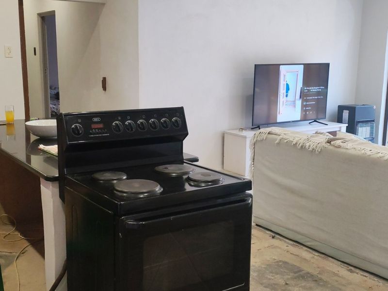Open plan living and kitchen area currently undergoing renovation with unfinished flooring and wall surfaces, featuring a breakfast bar and freestanding electric stove.