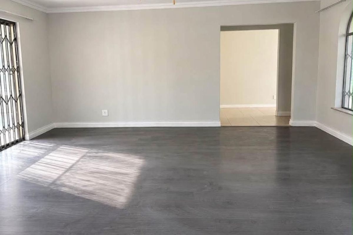 Spacious, light-filled living area featuring modern dark laminate flooring, a ceiling fan, and elegant crown molding, providing a clean and versatile blank canvas.