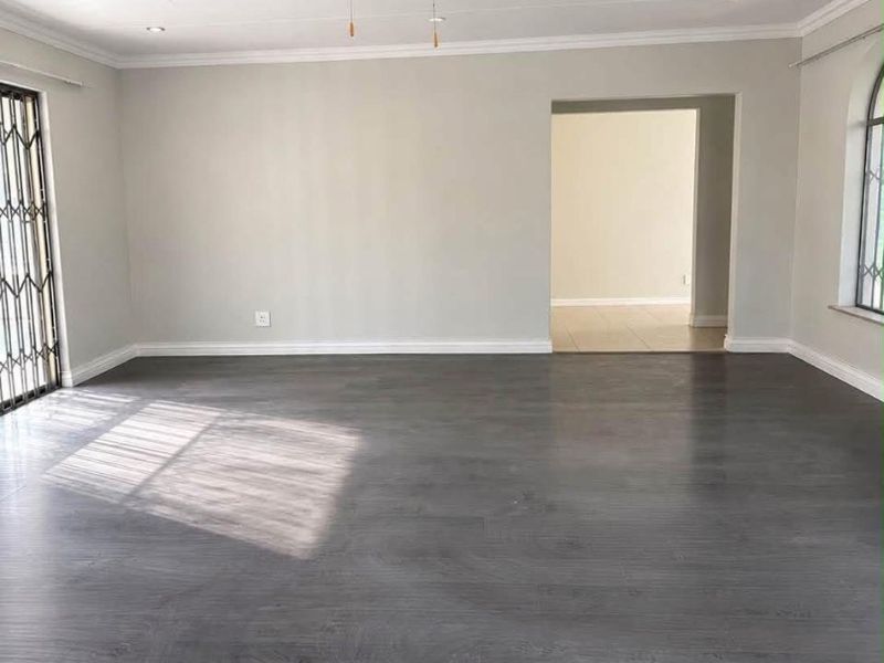 Spacious, light-filled living area featuring modern dark laminate flooring, a ceiling fan, and elegant crown molding, providing a clean and versatile blank canvas.