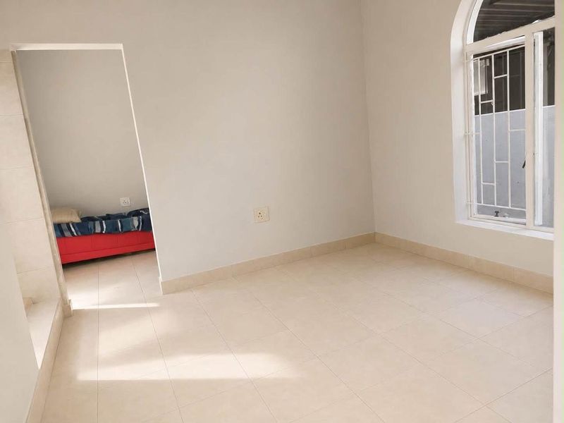 A bright, empty bedroom featuring neutral tiled flooring and an arched window with security bars, offering a clean canvas for personalization.