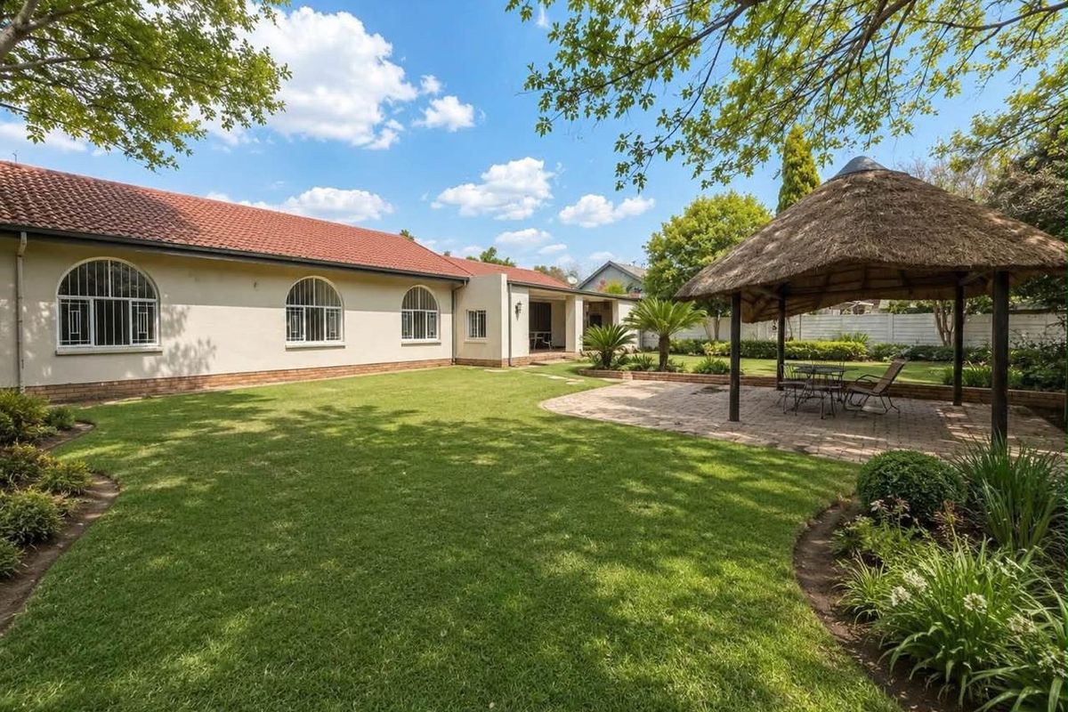 Spacious rear garden featuring a well-maintained lawn, a paved patio area, and a traditional thatched lapa, perfect for outdoor entertaining.