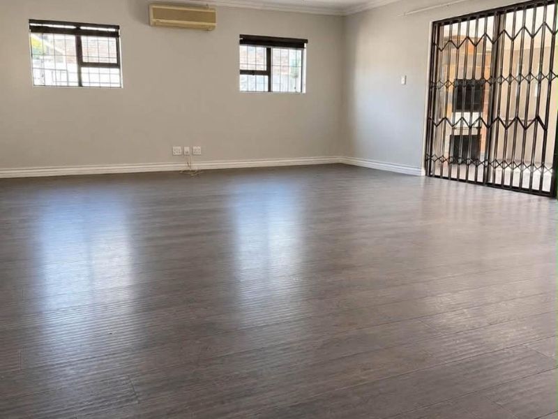 Spacious, empty living area featuring dark laminate flooring, a ceiling fan, wall-mounted air conditioning, and secure sliding door access to the patio.