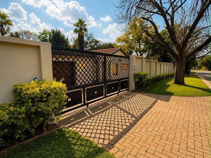Front view of the property featuring a secure metal driveway gate, perimeter wall, and well-maintained paved driveway with landscaped lawn.