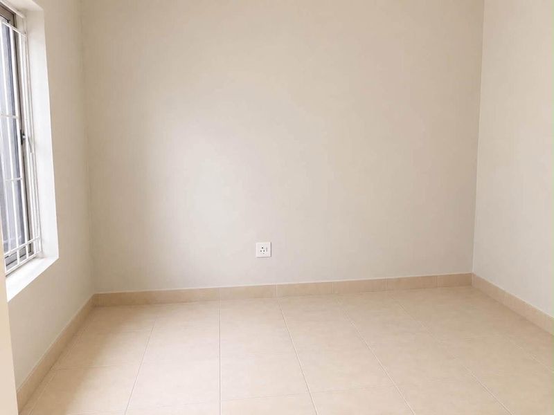 A clean, empty bedroom featuring neutral tiled flooring, a window with security bars, and a simple, well-maintained finish.