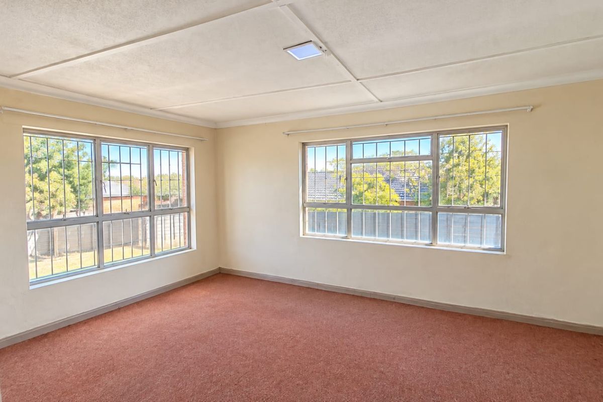 A spacious, empty bedroom featuring large windows with security bars, carpeted flooring, and a neutral color palette, ready for renovation or staging.