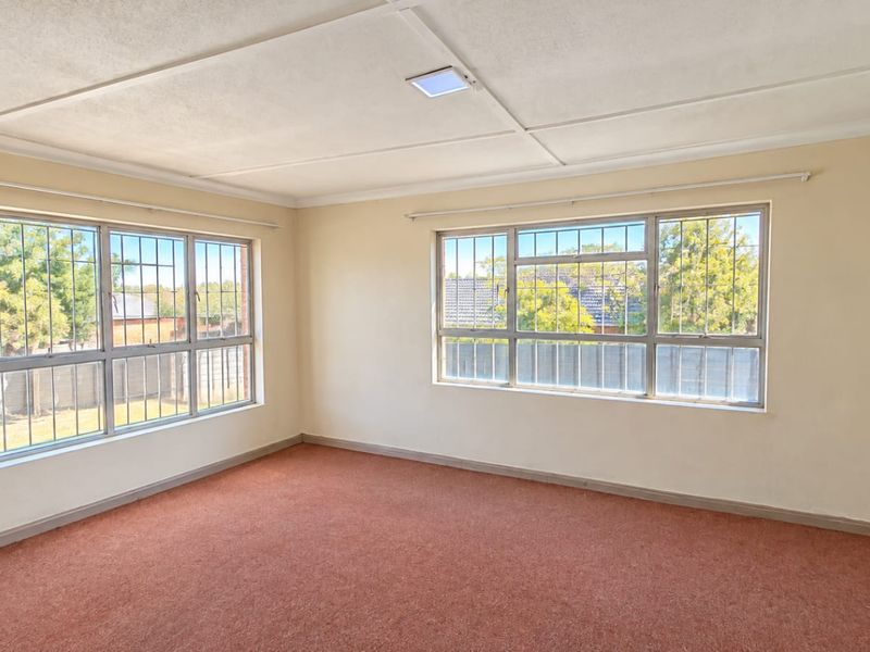 A spacious, empty bedroom featuring large windows with security bars, carpeted flooring, and a neutral color palette, ready for renovation or staging.