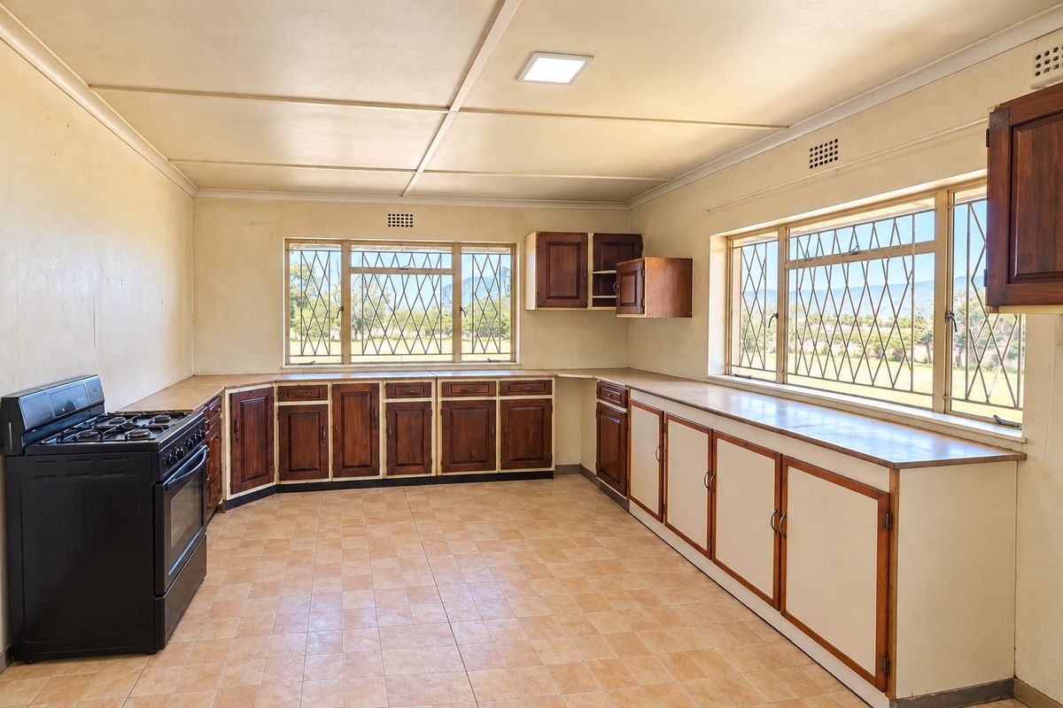 Spacious kitchen featuring extensive built-in wooden cabinetry, tiled flooring, and large windows with security bars, offering a functional layout ready for modernization.