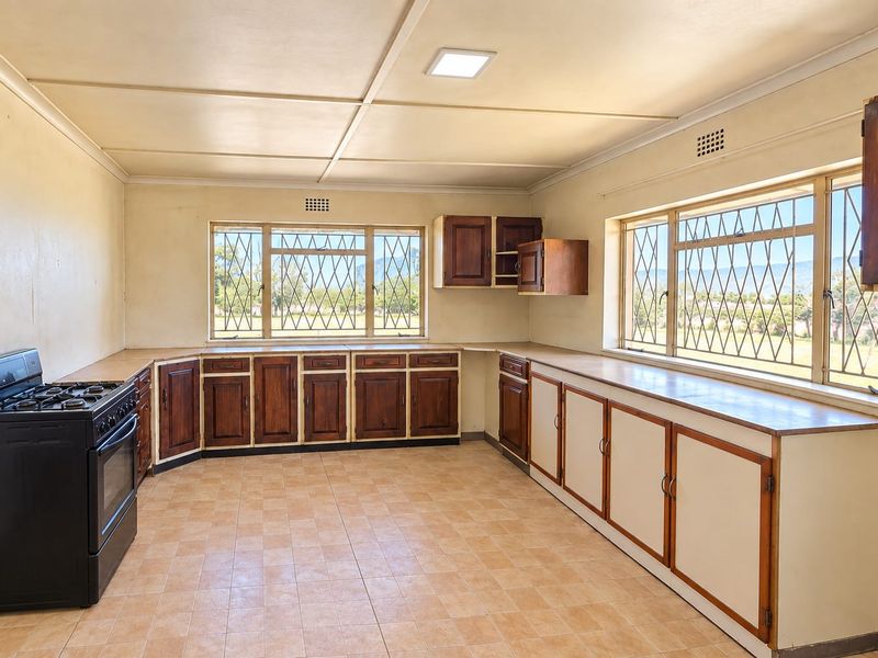 Spacious kitchen featuring extensive built-in wooden cabinetry, tiled flooring, and large windows with security bars, offering a functional layout ready for modernization.