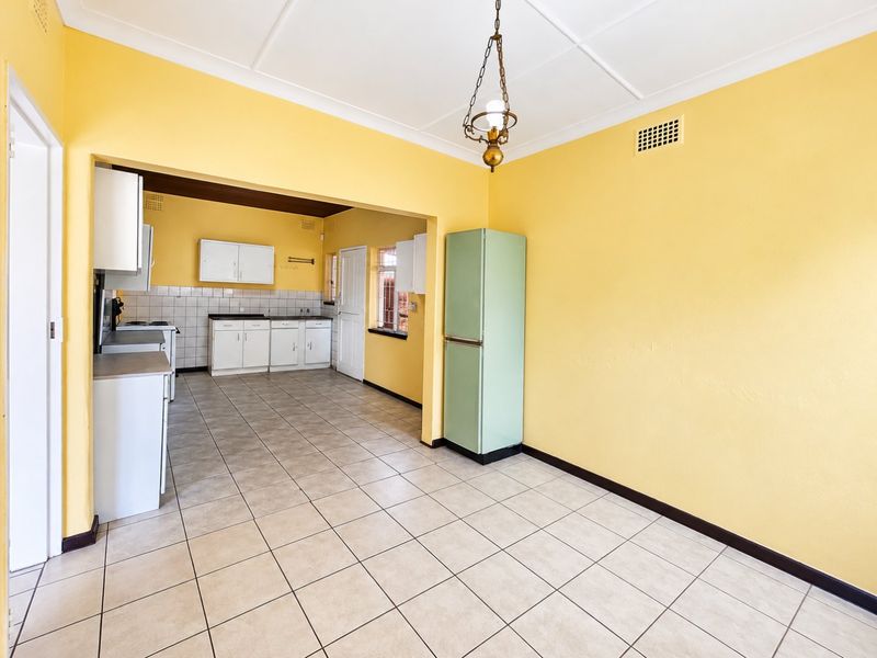 An open-plan kitchen and dining area featuring tiled flooring, built-in cabinetry, and a tiled backsplash, offering a functional space ready for modernization.