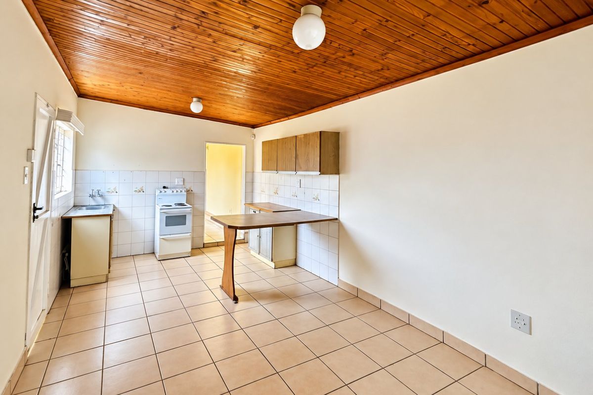 A functional, empty kitchen featuring tiled flooring, a timber ceiling, built-in cabinetry, and a tiled splashback, offering a blank canvas for modern renovation.