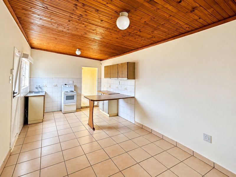 A functional, empty kitchen featuring tiled flooring, a timber ceiling, built-in cabinetry, and a tiled splashback, offering a blank canvas for modern renovation.
