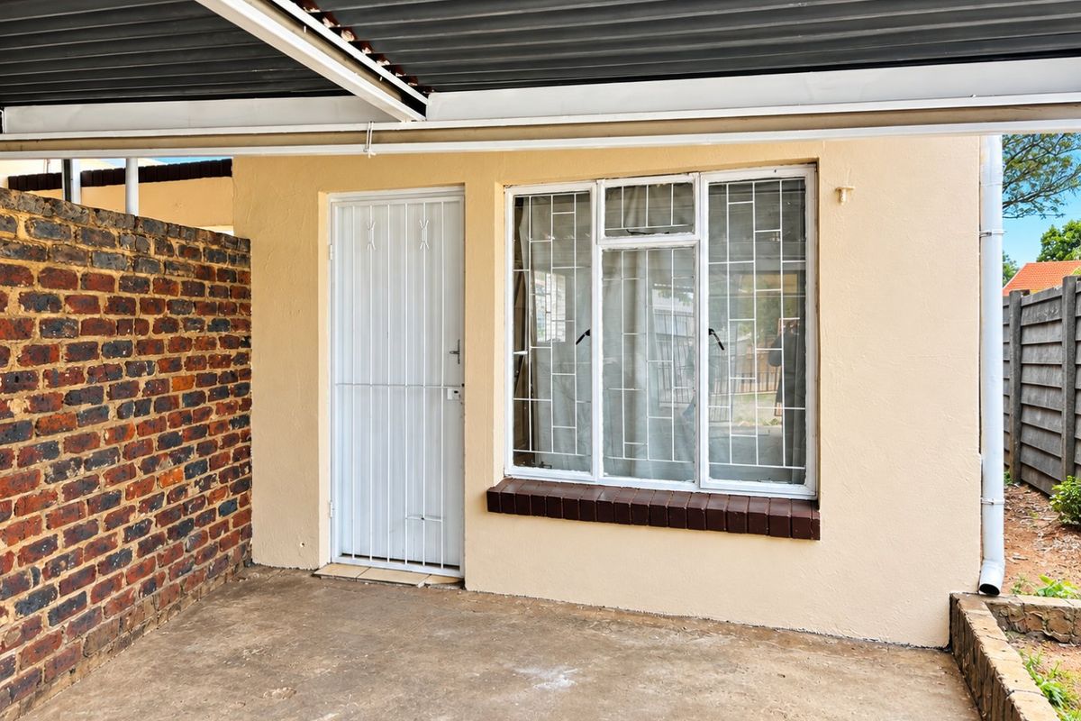 A covered patio area featuring a concrete floor, brick boundary wall, and secure window and door access, suitable for outdoor seating or utility use.