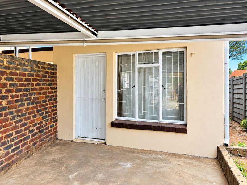 A covered patio area featuring a concrete floor, brick boundary wall, and secure window and door access, suitable for outdoor seating or utility use.