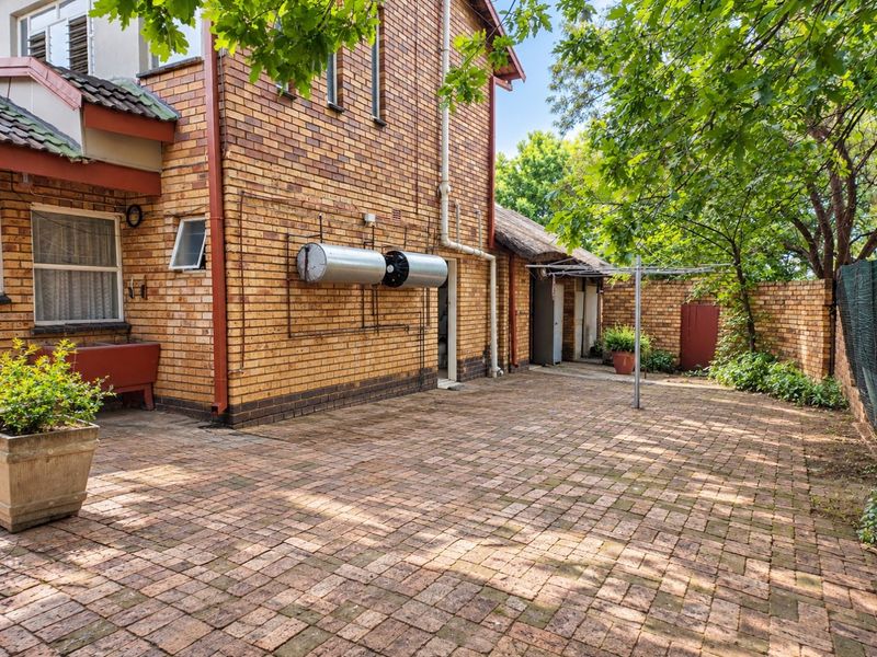 A paved rear courtyard area featuring facebrick walls, a mounted solar geyser system, and a functional laundry drying area.