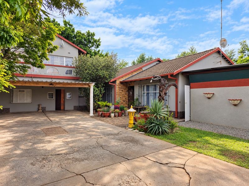 Front exterior view of the property featuring a large concrete driveway, tiled roof, and covered pergola entrance area.