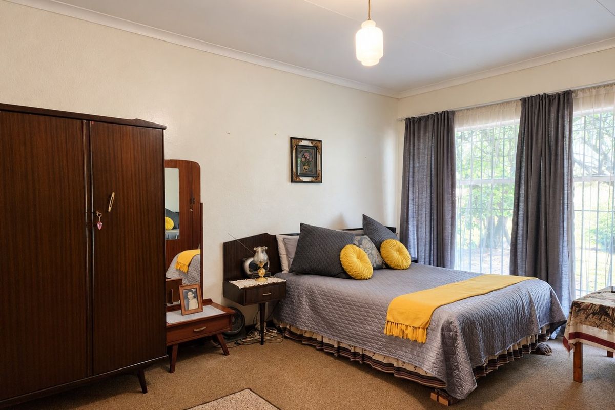 A well-lit bedroom featuring carpeted flooring, coved ceilings, and a large window fitted with security bars, offering a functional and comfortable living space.