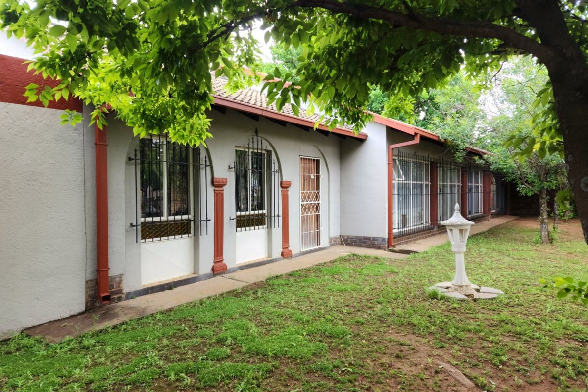 Rear view of the house featuring a concrete pathway, arched window frames with security bars, and a tiled roof set against a garden area.