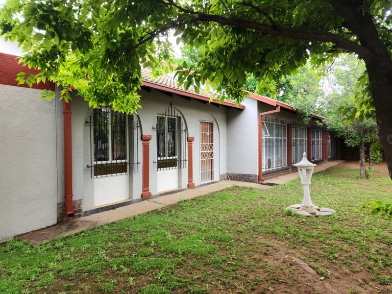 Rear view of the house featuring a concrete pathway, arched window frames with security bars, and a tiled roof set against a garden area.