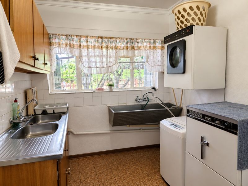 Functional laundry room featuring a double stainless steel sink, a wall-mounted concrete utility basin, built-in wooden cabinetry, and tiled splashbacks.