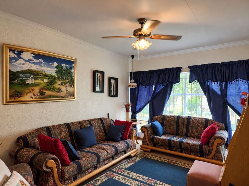 A comfortable living room featuring a ceiling fan, coved cornicing, and large windows fitted with security bars.