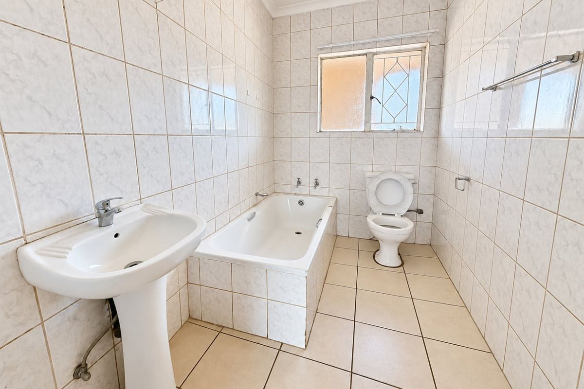 A functional, empty bathroom featuring a pedestal basin, built-in bathtub, and toilet with full-height wall tiling and neutral floor tiles.