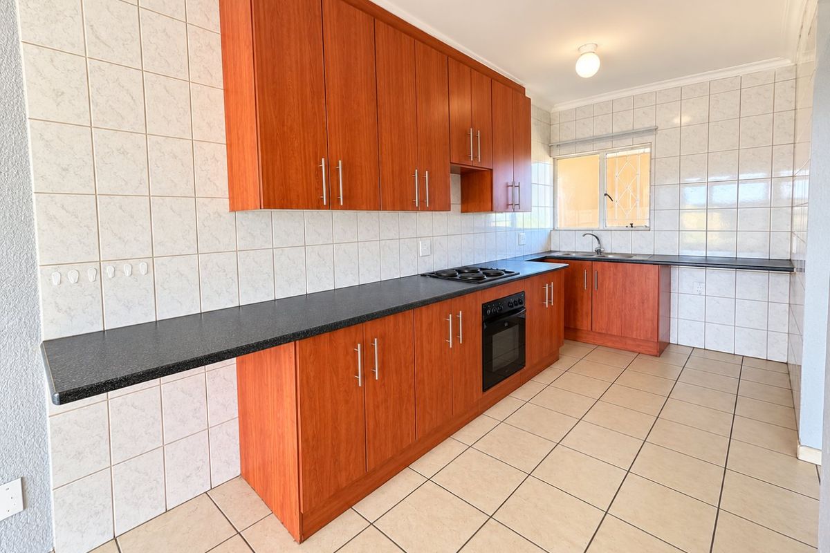 A functional kitchen featuring wood-finish cabinetry, dark laminate countertops, built-in oven and hob, and tiled surfaces throughout.