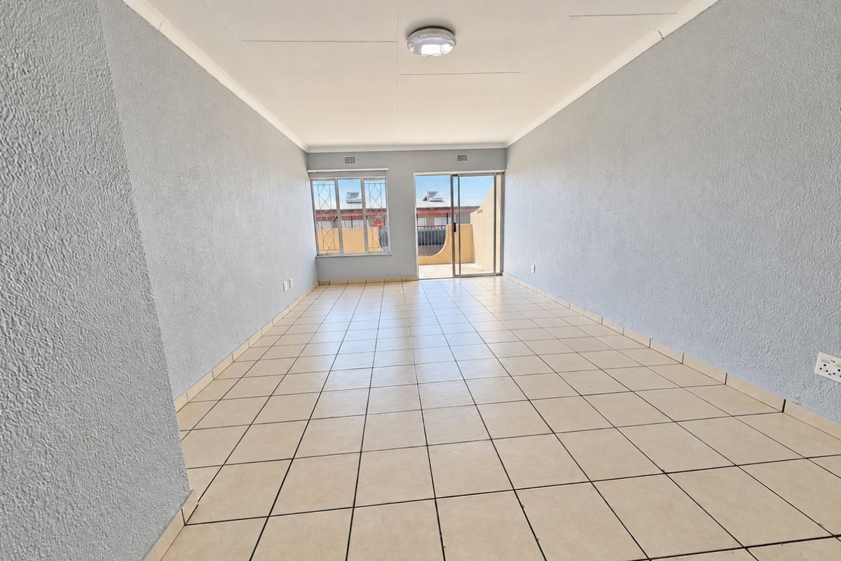 A spacious, empty living area featuring neutral tiled flooring, light-colored walls, and direct access to an outdoor patio through a sliding glass door.