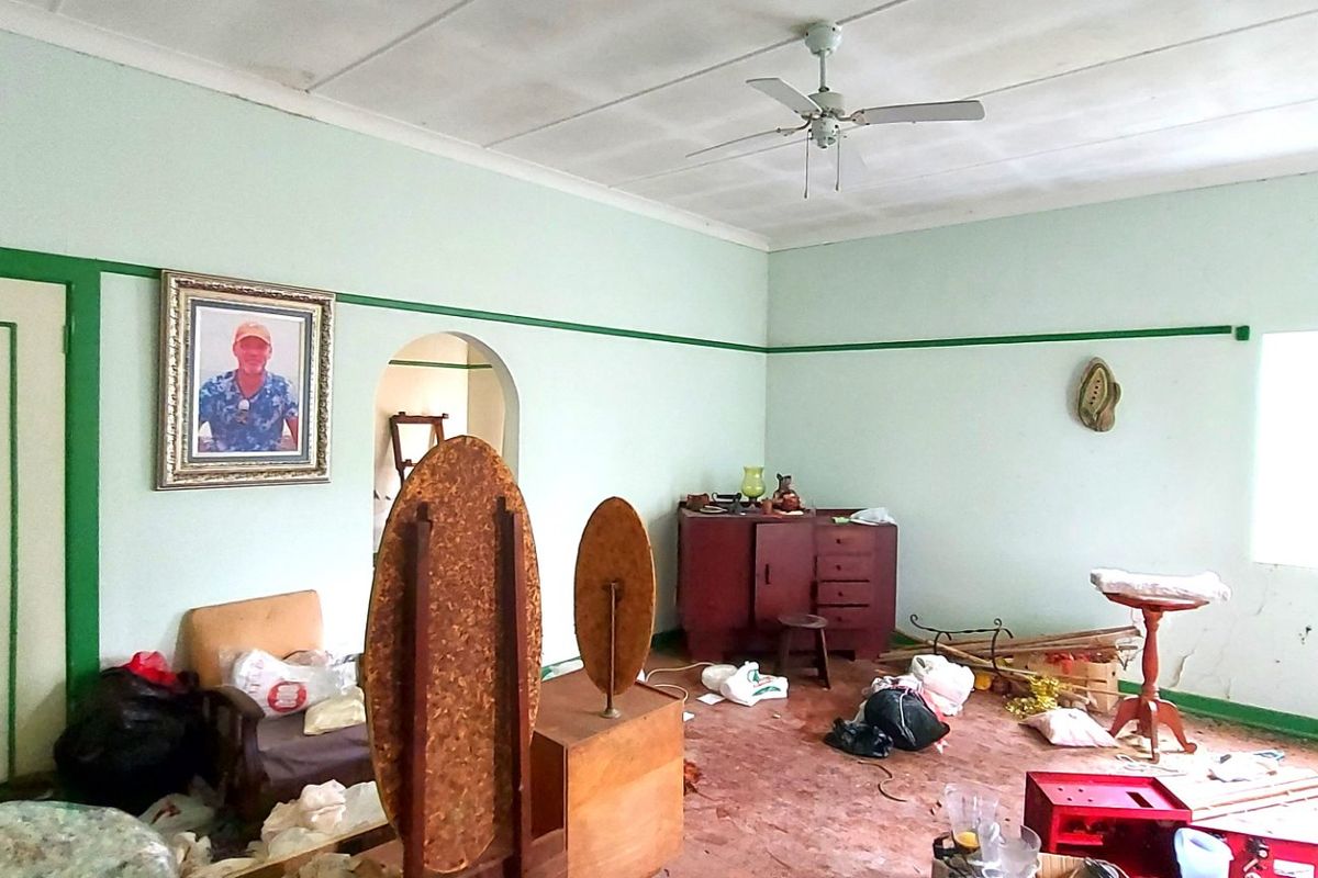 A living room featuring an archway, ceiling fan, and picture rail, currently requiring significant cosmetic updates and repairs to the walls and flooring.