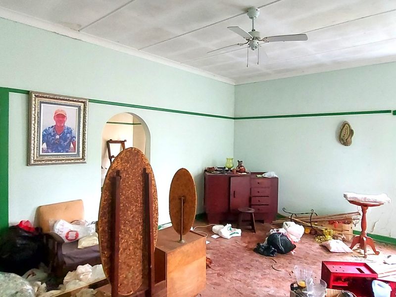 A living room featuring an archway, ceiling fan, and picture rail, currently requiring significant cosmetic updates and repairs to the walls and flooring.