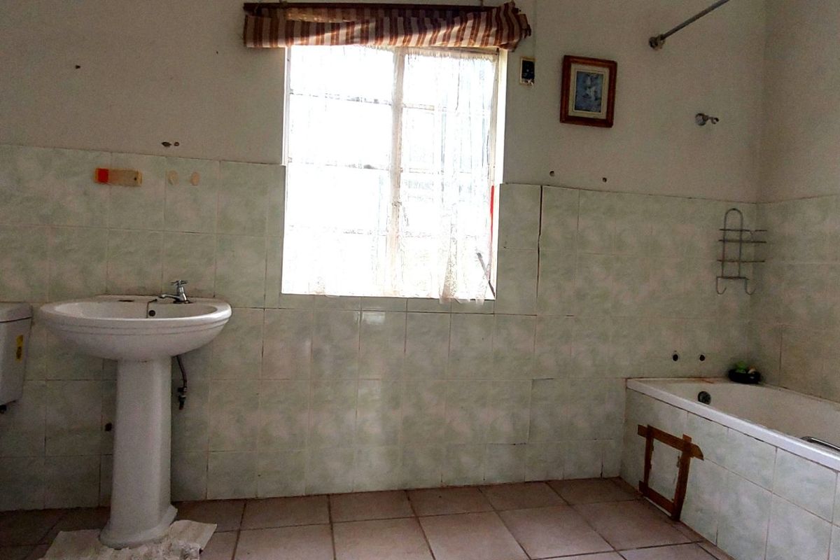 A dated bathroom featuring a pedestal basin, toilet, and bathtub with tiled walls and flooring, requiring cosmetic updates and repairs to the bathtub panel.