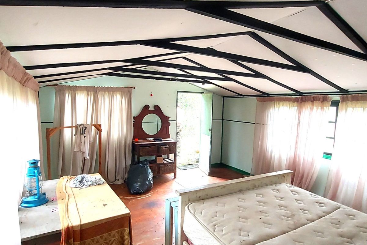 A bedroom featuring exposed ceiling beams and timber flooring, requiring cosmetic updates to improve the overall condition and aesthetic appeal.