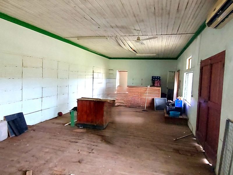 A spacious, vacant living area featuring timber flooring, a timber ceiling, and security-barred windows, requiring significant cosmetic refurbishment and ceiling repairs.