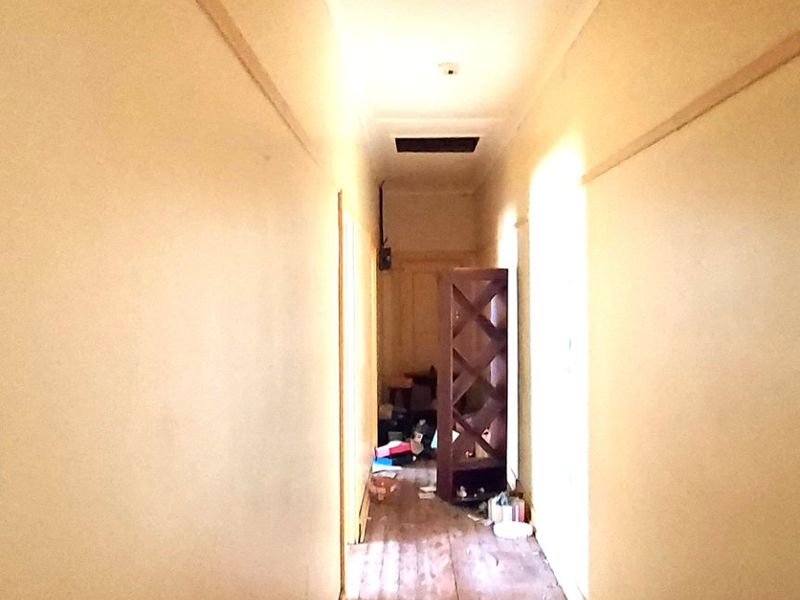 A narrow hallway featuring original timber flooring and a ceiling access hatch, requiring cosmetic updates and repairs to the ceiling.