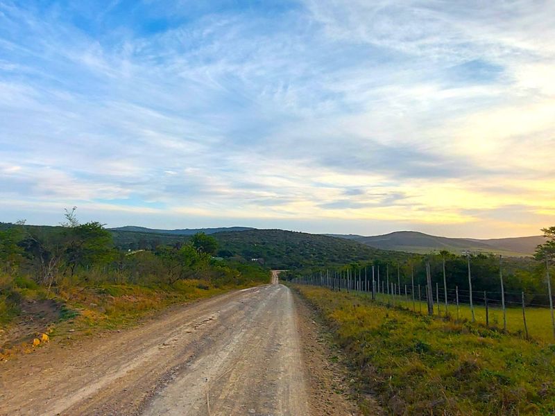 A scenic view of a rural dirt road stretching through open landscape with a wire fence and sunset sky.