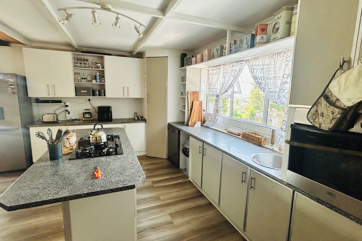 A functional kitchen featuring a central island with a gas hob, granite countertops, built-in oven, and ample cabinetry, finished with modern laminate flooring.