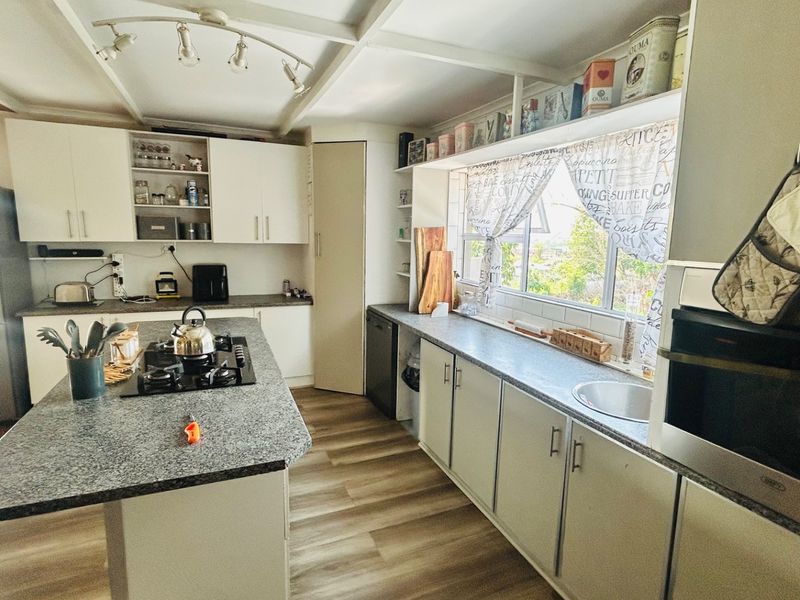 A functional kitchen featuring a central island with a gas hob, granite countertops, built-in oven, and ample cabinetry, finished with modern laminate flooring.