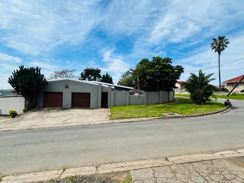 Street view of the property featuring a double garage with metal doors, a concrete driveway, and a surrounding perimeter wall.