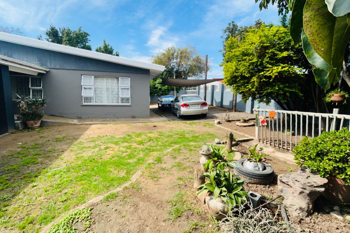 Rear exterior view of the property featuring a painted brick facade, a shade cloth carport, and a garden area with perimeter fencing.