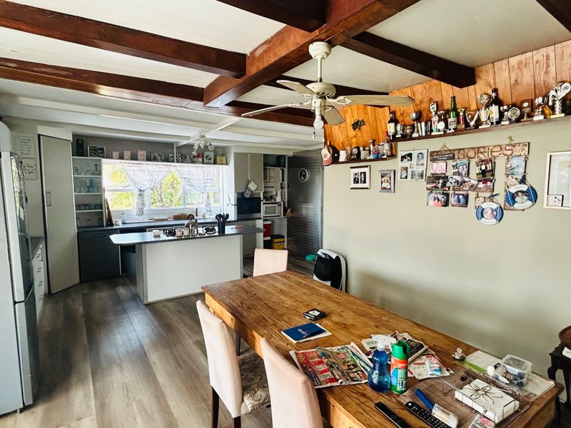 Open-plan kitchen and dining area featuring exposed timber ceiling beams, a central kitchen island, and timber-look flooring with a rustic aesthetic.