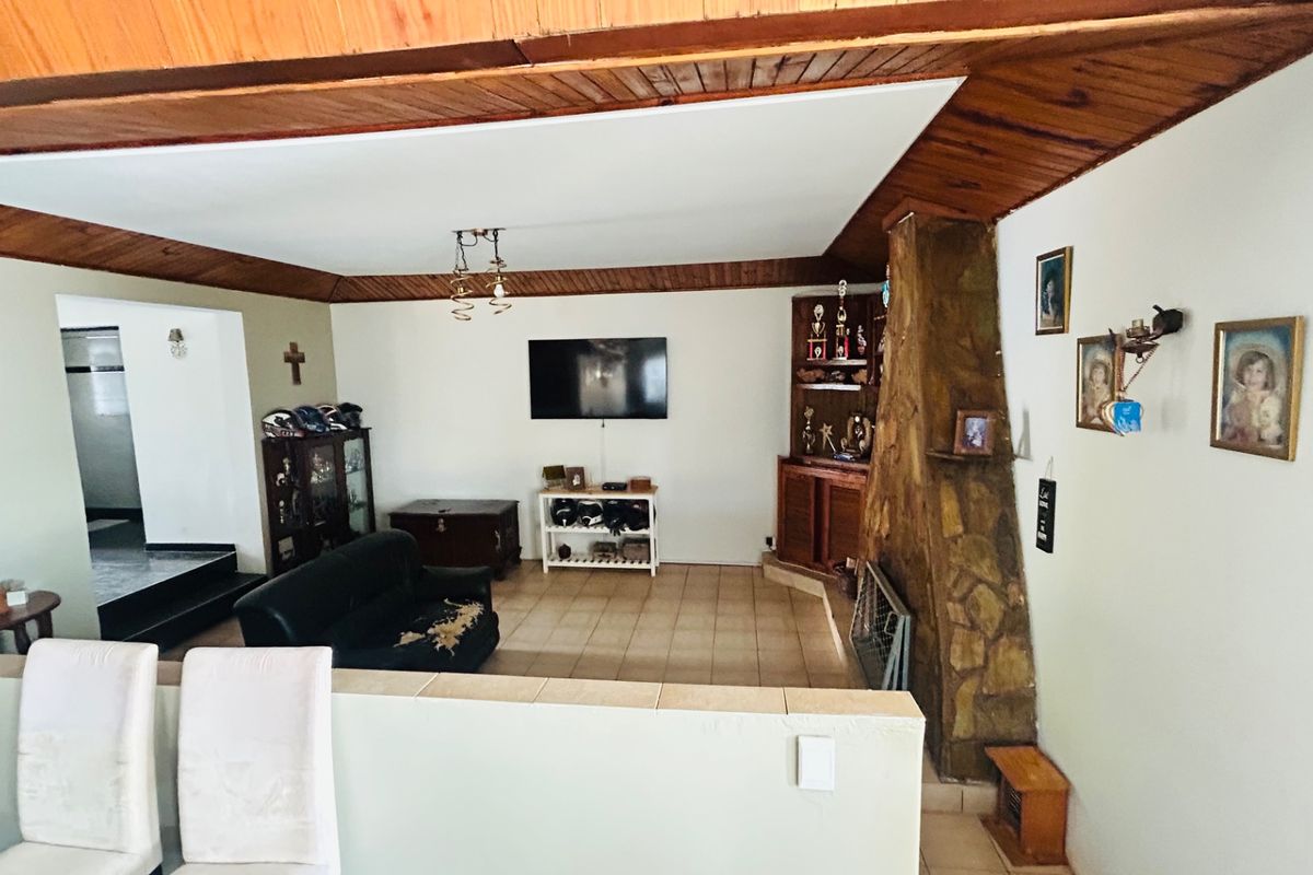 Spacious living room featuring a prominent stone fireplace, built-in cabinetry, and timber ceiling detailing, offering a dated aesthetic ready for modernization.