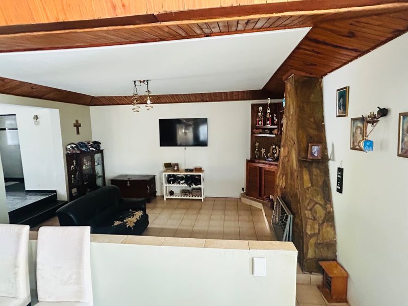 Spacious living room featuring a prominent stone fireplace, built-in cabinetry, and timber ceiling detailing, offering a dated aesthetic ready for modernization.